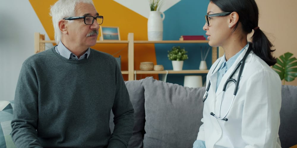 A doctor consulting with an elderly patient seated on a couch