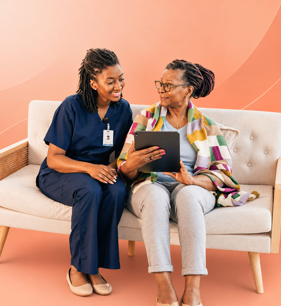 A LifeCare caregiver in navy scrubs sitting beside a smiling resident holding a tablet